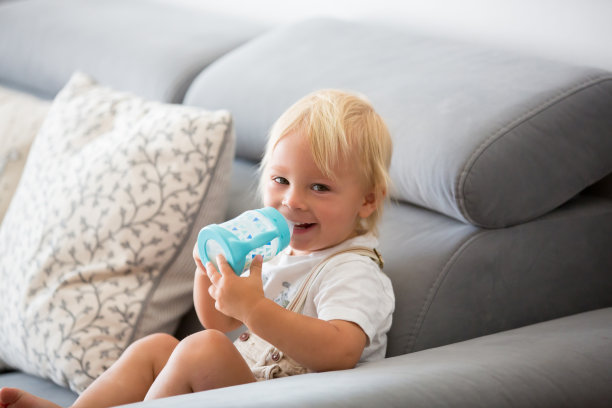 可爱的小男孩在阳光明媚的白色客厅里用奶瓶喝牛奶。图片下载