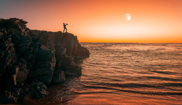 日落时，萨克斯管吹奏者在悬崖上演奏的剪影，背景是满月图片下载