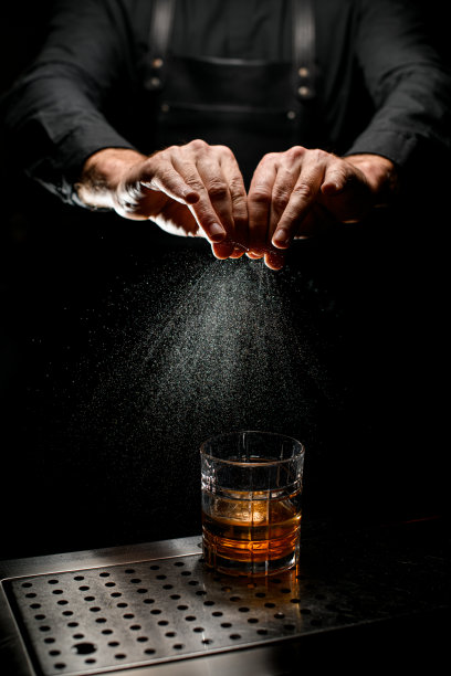 男性调酒师的手在黑色背景下从橘子皮中提取精油。图片下载