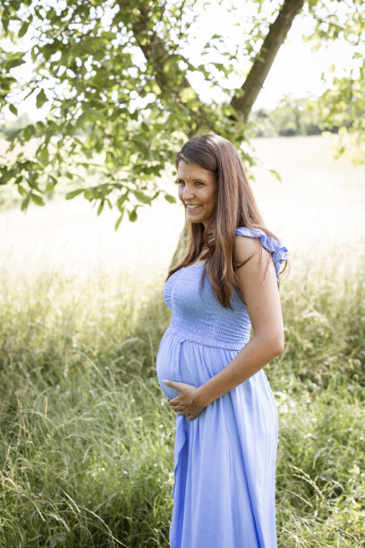 黑头发、蓝裙的年轻漂亮孕妇站在草地上图片下载