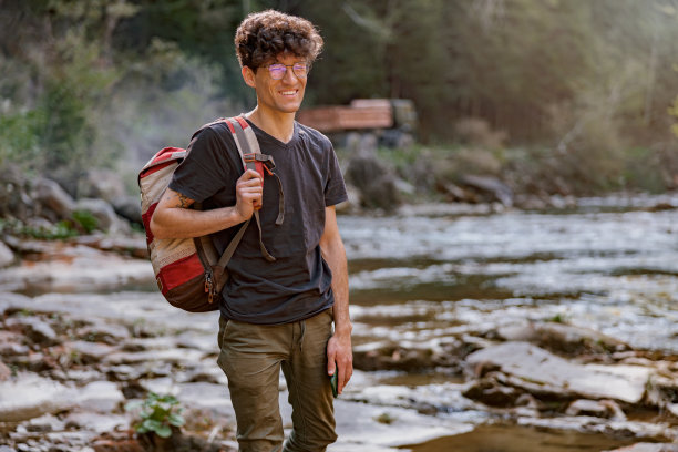 年轻开朗的男性旅行者在山间的河边散步的肖像。野生自然。图片下载
