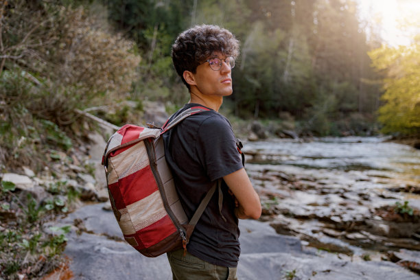 英俊的年轻男性徒步旅行者背着背包站在山中的河边。徒步旅行的概念。图片下载