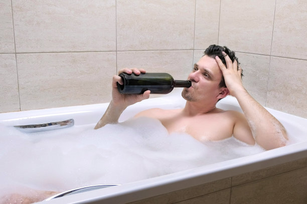 疲惫的30多岁男子在浴缸里喝着一瓶酒睡着了。图片下载