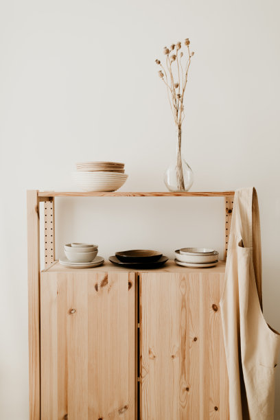 一个木制餐具柜，有陶瓷盘子和碗，干花插在玻璃花瓶里，上面有一条棉布围裙。图片下载