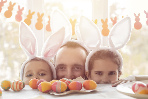 爸爸和女儿们一起玩耍，为复活节画彩蛋。幸福的一家人准备过复活节，女孩们戴着兔耳朵图片下载