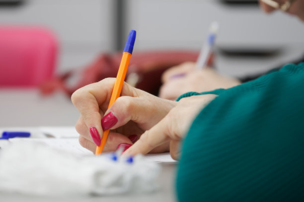 一位涂着红色美甲的女士用钢笔写下演讲内容的大纲、填写文件、合同或简历。没有脸。有选择性的重点图片下载