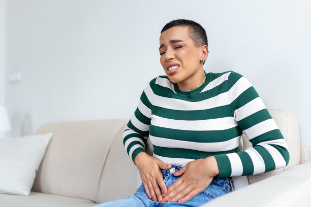 非洲裔美国女性以痛苦的表情握住肚子遭受经期疼痛，躺在家里的床上伤心，有肚子抽筋的女性健康观念图片下载
