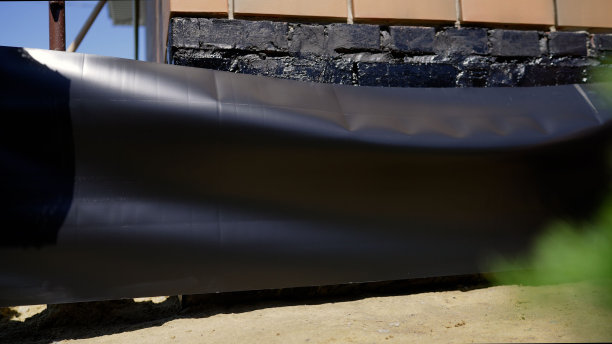 砖房的沥青保温材料一层底漆用薄膜水化。用黑色砂浆为房屋地基防水。用防水沥青密封的房子的砖墙。图片下载