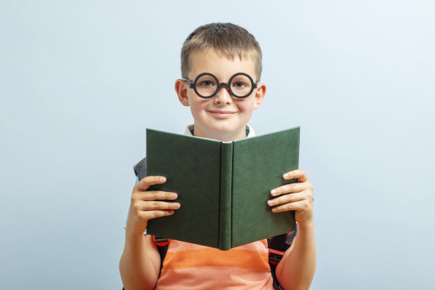 戴眼镜的小男生正在看一本蓝色背景的书。教育与办学理念图片下载