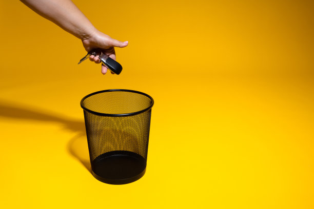 手把车钥匙扔进垃圾桶。汽车钥匙被扔进办公室的废纸篓里。燃油涨价概念图片下载
