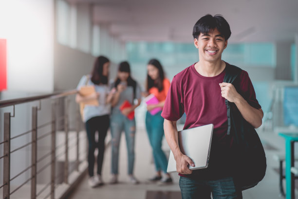一名亚洲学生手持笔记本电脑站在大学校园，快乐的教育交流交流。图片下载