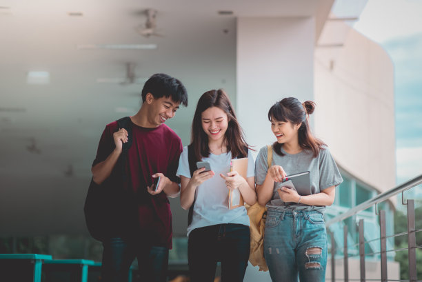 一群亚洲学生在大学里一边走路一边用智能手机，交流交流。图片下载