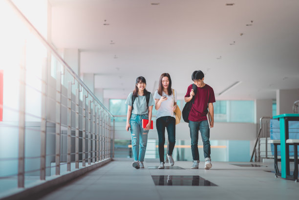 一群亚洲学生在大学里一边走路一边用智能手机，交流交流。图片下载