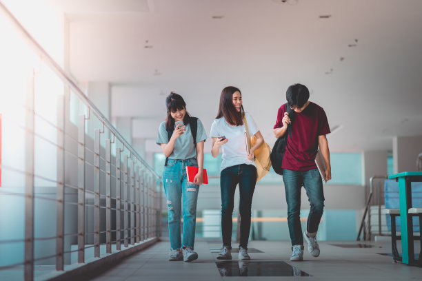 一群亚洲学生在大学里一边走路一边用智能手机，交流交流。图片下载