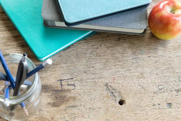 边缘的蓝绿色和灰色的书，苹果和一罐铅笔在质朴的木头书桌图片下载