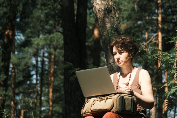 一个晴朗炎热的夏天，女人在森林里的笔记本电脑上工作图片下载