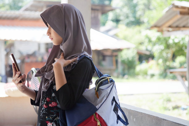 戴头巾的亚洲穆斯林女孩背着背包使用手机图片下载