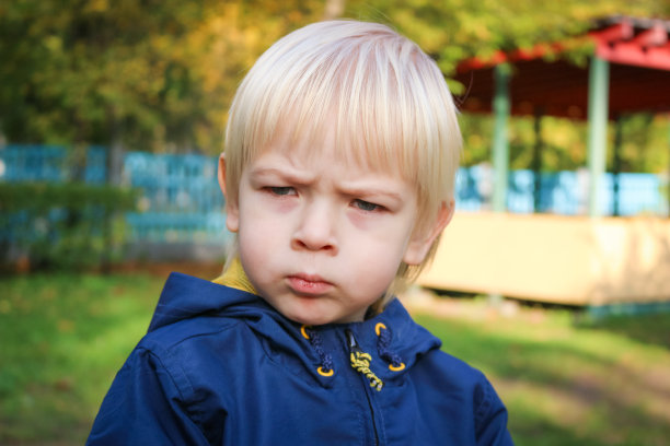 幼小严肃的孩子在秋天的公园里散步。可爱的白人小男孩与深思熟虑的表情在蓝色的眼睛特写。金发小男孩看着别处，情绪强烈，脸上带着悲伤。图片下载