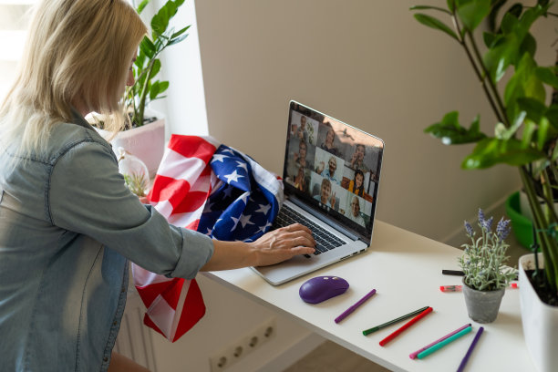 快乐的年轻女学生举着美国国旗，在客厅里用黑屏笔记本电脑学习。居家国际教育，远程授课，网站因新冠疫情隔离图片下载