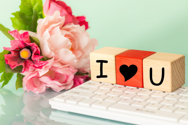I HEART U, I love you，在互联网上用于电子邮件问候或对所爱的人的爱的宣言的缩写。在电脑键盘和一束鲜花的背景下，木块上的铭文图片下载