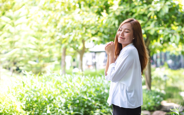 一名年轻女子闭上眼睛在公园里享受图片下载