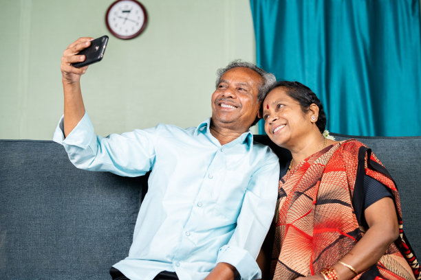 快乐的老年夫妇坐在家里的沙发上用手机自拍-家庭的概念，团聚和联系。图片下载