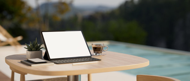 游泳池附近的木制桌子上的便携式数字平板电脑模型和东西图片下载