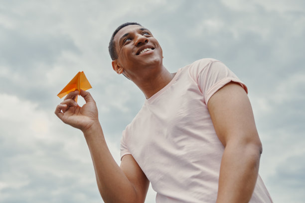 低角度视角英俊的混血男子手持纸飞机与天空为背景图片下载
