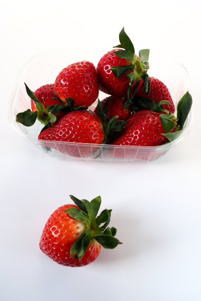 成熟的草莓放在白色背景的塑料包装里。美味新鲜的浆果装在容器里出售给顾客。保持食物新鲜。健康食品。从容器里拿出一颗草莓图片下载