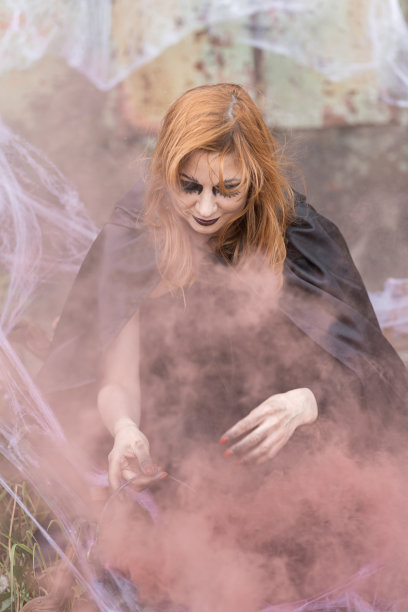 迷人的美丽的女人在万圣节服装黑色斗篷和可怕的化妆。年轻的女孩在一个女巫打扮为一个聚会制作仙女药水拿着黑色灯笼。图片下载