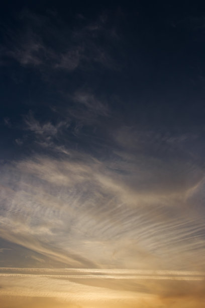 夕阳西下的天空，云朵被太阳照亮。尾迹和羽状云。图片下载