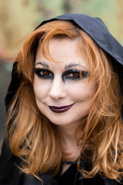 迷人的美丽的女人在万圣节服装黑色斗篷和可怕的化妆。年轻的女孩在一个女巫打扮为一个聚会制作仙女药水拿着黑色灯笼。图片下载