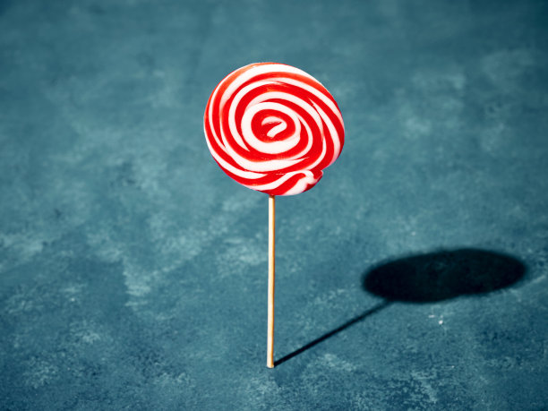 白色和红色旋转的糖果棒棒糖站在蓝色的背景。夏天的概念。图片下载