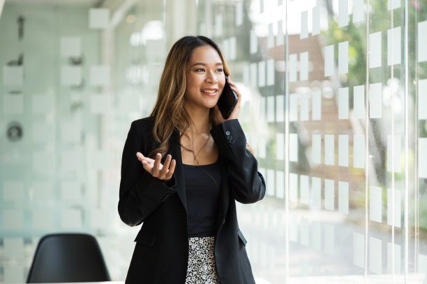 年轻的亚洲女商人站在窗边打电话。图片下载