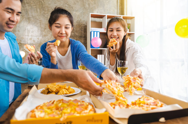 年轻的创业亚洲人坐在办公室一起吃披萨。坐在办公室桌子旁吃午饭的上班族。图片下载