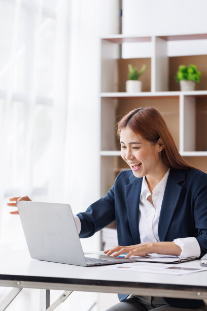 快乐兴奋的年轻亚洲女性在家拿着笔记本电脑坐在家里的办公室里，情绪激动的女孩感到高兴和快乐图片下载