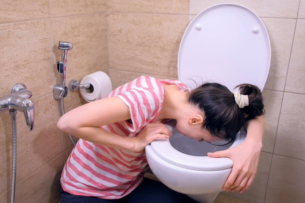 年轻的孕妇累了，坐在家里的地板上，在厕所里呕吐。图片下载