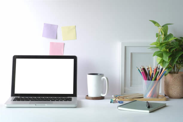 舒适的工作空间，笔记本电脑，咖啡杯，盆栽植物和文具装饰在白色的桌子上。家庭办公室。图片下载