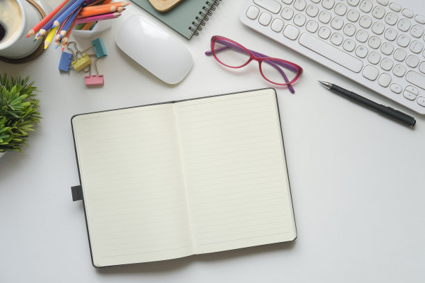 白色的办公桌上平放着笔记本、眼镜、咖啡杯和盆栽植物。图片下载