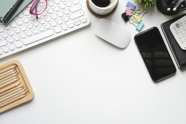 白色桌子上有智能手机、咖啡杯、计算器和办公用品。前视图。图片下载