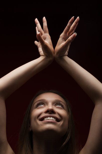 深红色背景下的可爱女孩。深色头发的女士特写肖像抬头举起手。图片下载
