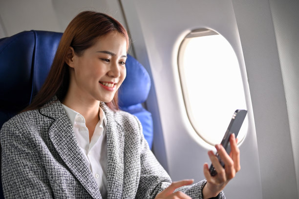 美丽的亚洲女商人使用智能手机检查她的会议安排在飞机上。图片下载