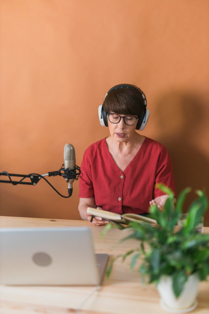 成熟的女人为她的在线节目制作播客录音。有吸引力的商业女性使用耳机前面的麦克风广播图片下载