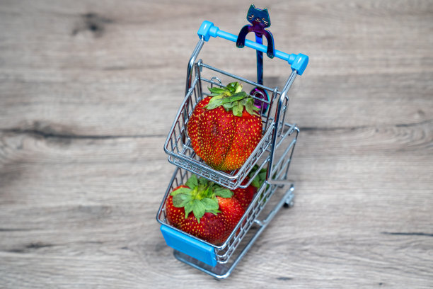 超市购物车，手推车上放着草莓，放在木桌上，概念购买的产品图片下载