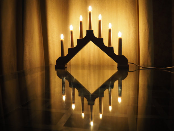 Schwibbogen拱门灯具，玻璃桌上的三角形烛台。黄色背景。晚上，有浪漫、喜庆、宗教或神秘的气氛。燃烧着像烛光一样的灯泡。图片下载