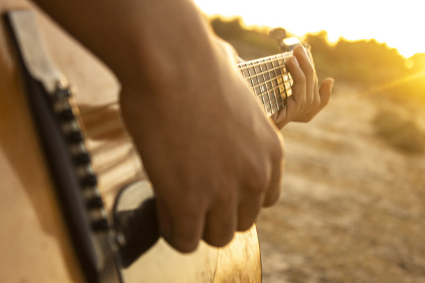 吉他和日落。在日落时弹原声吉他。在日落时播放音乐。和朋友一起欣赏日落，在黄金时间弹吉他。吉他背景图片下载