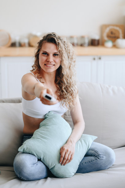 一个穿着白色运动上衣的女孩的垂直照片。女孩通过开关遥控器看电视。图片下载