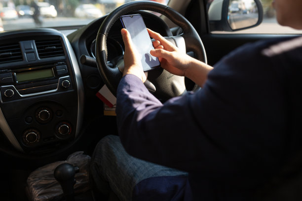 商人在开车时用手机打字发短信。一名男子一边开车一边用手机看地图。道路安全与粗心的概念。图片下载