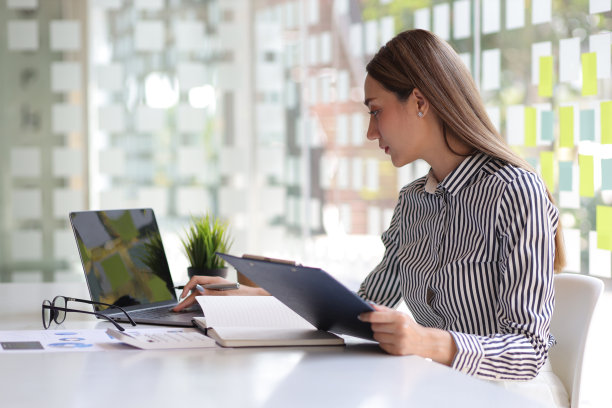 商务女性工作的财务报告的计算器和笔记本电脑的办公桌在办公室。图片下载