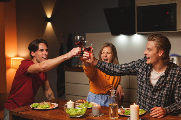 三个兴高采烈的年轻朋友，两男一女，在家里的庆祝晚宴上用红酒干杯图片下载
